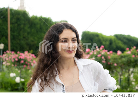 Beautiful successful 35-year-old woman in white shirt walking in the park among roses Beautiful successful 35-year-old woman in white shirt walking in the park among roses 104433837