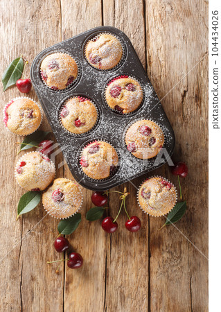 Homemade cherry muffins in cupcake liners and fresh cherries in the background. Vertical top view Homemade cherry muffins in cupcake liners and fresh cherries in the background. Vertical top view 104434026
