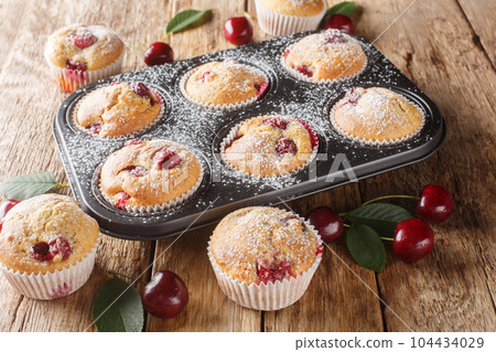 Muffins with fresh cherries sprinkled with powdered sugar close-up in a muffin tin. Horizontal 104434029
