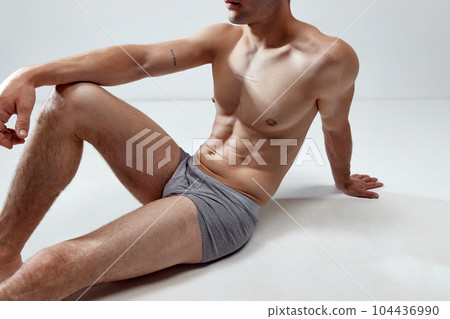 Cropped image of young man with muscular, relief, fit, strong body posing on floor in underwear against grey studio background 104436990