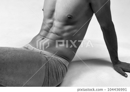 Black and white cropped image of male muscular, relief, fit, strong body. Model posing on floor in underwear Black and white cropped image of male muscular, relief, fit, strong body. Model posing on floor in underwear 104436991
