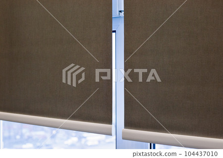 Roller blinds closeup on the window. Selective fokus. Motorized roller shades. Gray color, texture material. Two fabric webs through an intermediate bracket. Roller blinds closeup on the window. Selective fokus. Motorized roller shades. Gray color, texture material. Two fabric webs through an intermediate bracket. 104437010