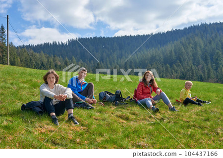 Happy family sitting on grass outdoors in park. happy young family spending time outdoor on a summer day Happy family sitting on grass outdoors in park. happy young family spending time outdoor on a summer day 104437166