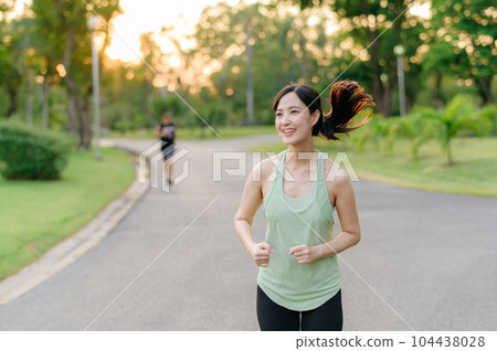 Fit Asian young woman jogging in park smiling - Stock Photo