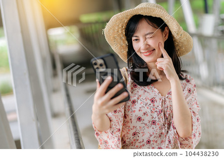 young asian woman traveler with weaving basket selfie with mobile phone and standing on overpass. Journey trip lifestyle, world travel explorer or Asia summer tourism concept. young asian woman traveler with weaving basket selfie with mobile phone and standing on overpass. Journey trip lifestyle, world travel explorer or Asia summer tourism concept. 104438230