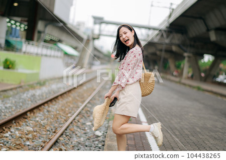 young asian woman traveler with weaving basket happy smiling looking to a camera beside train railway. Journey trip lifestyle, world travel explorer or Asia summer tourism concept. young asian woman traveler with weaving basket happy smiling looking to a camera beside train railway. Journey trip lifestyle, world travel explorer or Asia summer tourism concept. 104438265