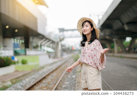 young asian woman traveler with weaving basket happy smiling looking to a camera beside train railway. Journey trip lifestyle, world travel explorer or Asia summer tourism concept. 104438273