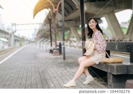 young asian woman traveler with weaving basket waiting for train in train station. Journey trip lifestyle, world travel explorer or Asia summer tourism concept. 104438278