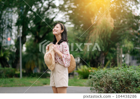 Portrait of asian young woman traveler with weaving hat and basket happy smile on green public park nature background. Journey trip lifestyle, world travel explorer or Asia summer tourism concept. 104438286