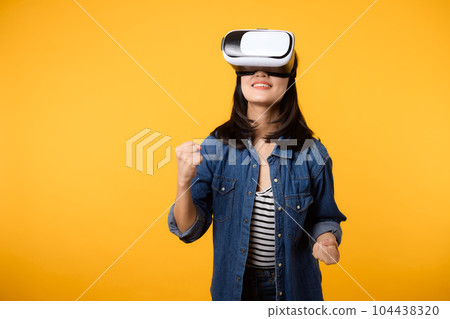 Young asian woman happy success wearing virtual reality headset game entertainment isolated on yellow background. Winner of cyber future video game concept. 104438320