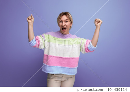 charming blond young woman shouting joyfully from victory holding her hands up on purple background 104439114