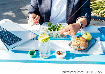 Healthy food concept: closeup woman eating from lunch box with healthy wholemeal burger bun, salad with fresh vegetables on the wooden picnic table outdoors. Balanced portion for weight loss diet. Healthy food concept: closeup woman eating from lunch box with healthy wholemeal burger bun, salad with fresh vegetables on the wooden picnic table outdoors. Balanced portion for weight loss diet. 104439222