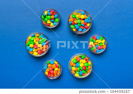 different colored round candy in bowl and jars. Top view of large variety sweets and candies with copy space different colored round candy in bowl and jars. Top view of large variety sweets and candies with copy space 104439287
