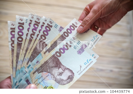 Money of Ukraine. Stack of ukrainian hryvnia banknotes in hands on wooden table. Hryvnia 1000 uah 104439774