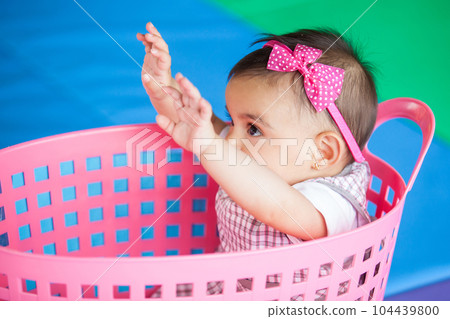Beautiful ten months baby girl playing in a pink basket. Early stimulation for toddlers concept. Beautiful ten months baby girl playing in a pink basket. Early stimulation for toddlers concept. 104439800