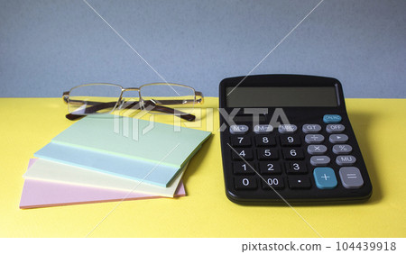 Close-up of a business workplace with colorful stickers, a calculator and glasses Close-up of a business workplace with colorful stickers, a calculator and glasses 104439918