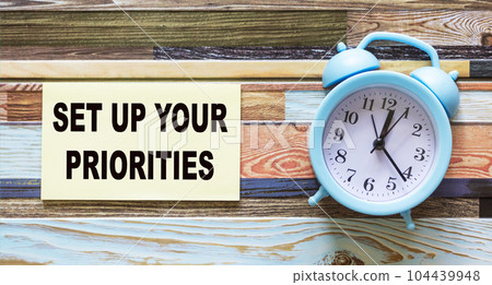 White notepad with text Set up your priorities , color background with alarm clock 104439948
