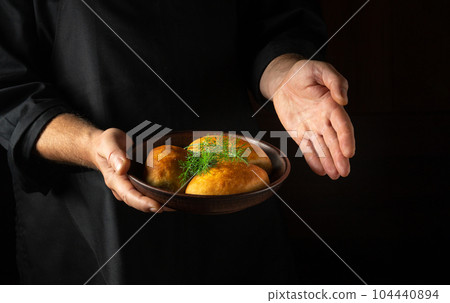 The baker presents in his hand a plate of freshly baked buns or dill pies. Free black space for menu or recipe. 104440894