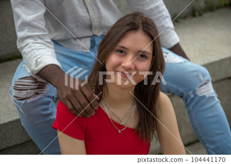 girl sitting between the legs of a black boy with his hand on her shoulder 104441170