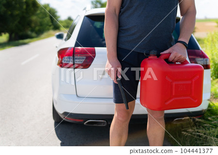A man is holding a red can next to a white car. Stop to refuel, problems on the road with refueling. A man is holding a red can next to a white car. Stop to refuel, problems on the road with refueling. 104441377