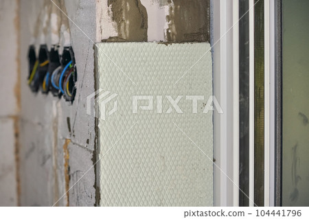 White polystyrene foam board insulation on a bare wall next to window - closeup detail during house construction White polystyrene foam board insulation on a bare wall next to window - closeup detail during house construction 104441796