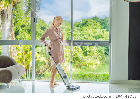 Young pregnant woman enjoys cleaning her house. Easy cleaning with a wireless vacuum cleaner. Pregnant woman cleaning floor with handheld vacuum cleaner. Modern easy cleaning 104442715
