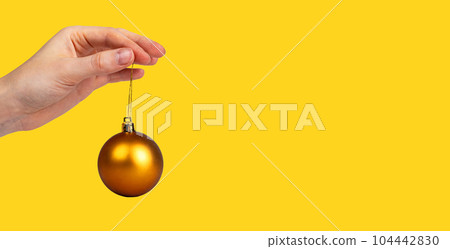 Gold brown Christmas ball, bauble, ornament on string, hanging in women hand. Yellow monochrome banner 104442830