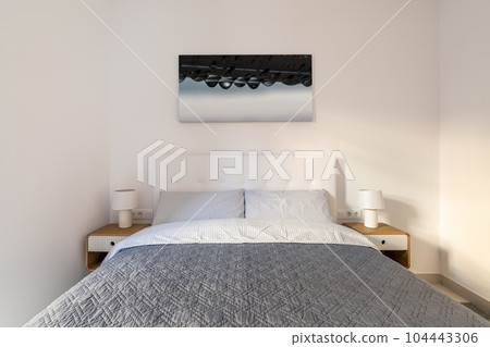 Double bed in the bedroom with a picture on the wall and stylish bedside tables in light colors. The concept of a compact room in a honeymoon hotel. Copyspace Double bed in the bedroom with a picture on the wall and stylish bedside tables in light colors. The concept of a compact room in a honeymoon hotel. Copyspace 104443306