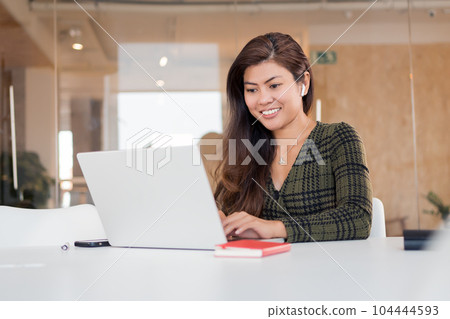 Smiling woman working on laptop in office 104444593