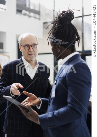 African american employee checking shirt inventory on tablet computer for elderly customer in shopping centre. Senior client buying formal clothes and fashionable accessories in modern boutique African american employee checking shirt inventory on tablet computer for elderly customer in shopping centre. Senior client buying formal clothes and fashionable accessories in modern boutique 104445423