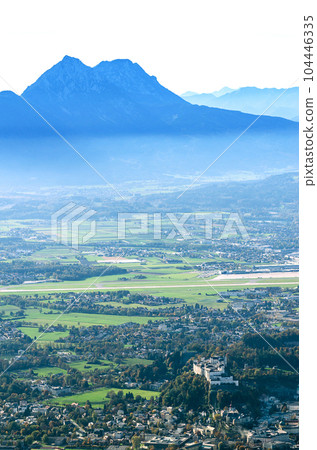Salzburg basin as seen from the Gaisberg mountain. City of Salzburg in Austria with Hohensalzburg Fortress, behind the city a part of the airport, and in the distance the mountain range Chiemgau Alps. 104446335
