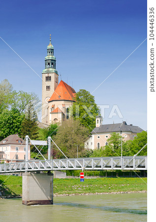 Muelln, a neighborhood in Salzburg, Austria. Pedestrian bridge Muellner Steg over Salzach river, a connection to the right old town of Salzburg. On the hill Muelln Church, the Catholic parish church. 104446336