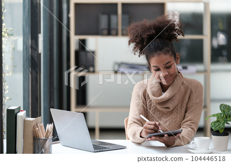 American African Woman working in the office with computer phone and Tablet. American African Woman working in the office with computer phone and Tablet. 104446518