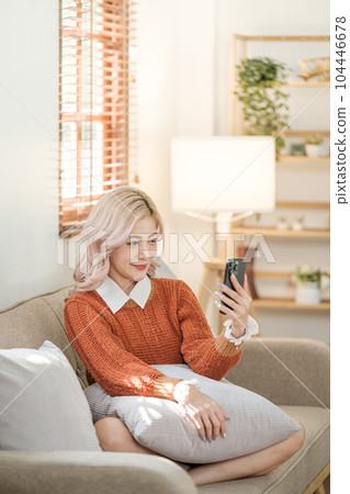 Young asian woman using a smart phone sitting on the sofa in the room. Order some online shopping. Young asian woman using a smart phone sitting on the sofa in the room. Order some online shopping. 104446678