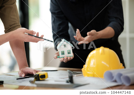 Engineers consulting team close up to design building blueprints paper for clients with building models to work at office. 104447148