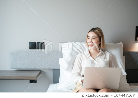 Young beautiful asian woman playing laptop on a bed. 104447167