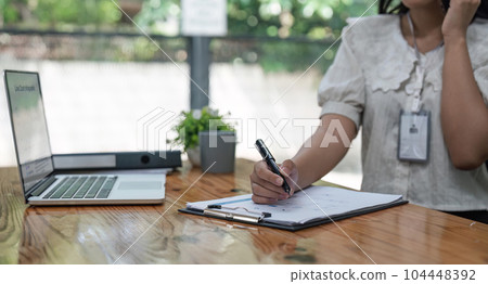Happy young asian woman talking on the mobile phone and while sitting at working place in office Happy young asian woman talking on the mobile phone and while sitting at working place in office 104448392