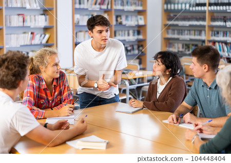 Schoolboy talking about his favorite book. Positive teenage students and female teacher discussing in library Schoolboy talking about his favorite book. Positive teenage students and female teacher discussing in library 104448404