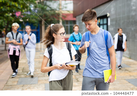 Teen schoolmates with backpacks and workbooks walking to college Teen schoolmates with backpacks and workbooks walking to college 104448477