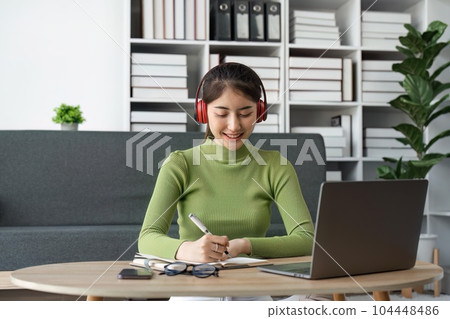 Young beautiful Happy Asian woman using laptop taking notes at home 104448486