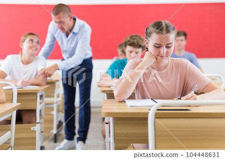 Teen girl listening to lecturer and writing in notebook in classroom Teen girl listening to lecturer and writing in notebook in classroom 104448631