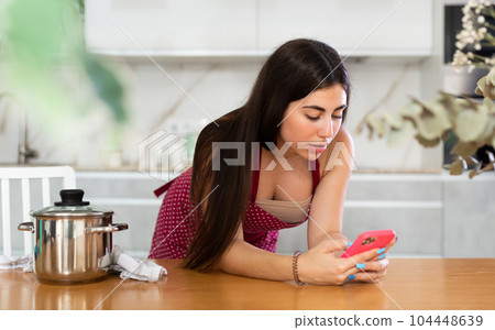 Young woman in apron reads message on phone 104448639