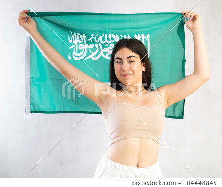 Happy young woman with flag of Saudi Arabia against unicoloured background Happy young woman with flag of Saudi Arabia against unicoloured background 104448845