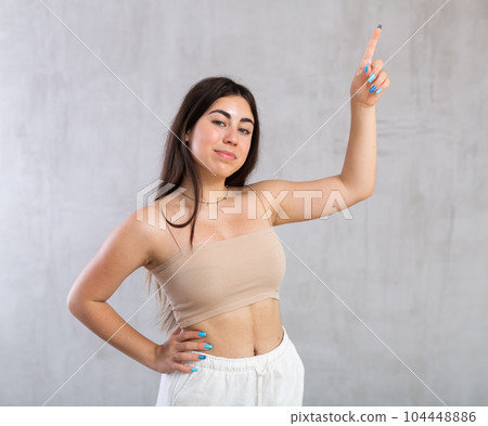 Young woman pointing up standing against the wall 104448886