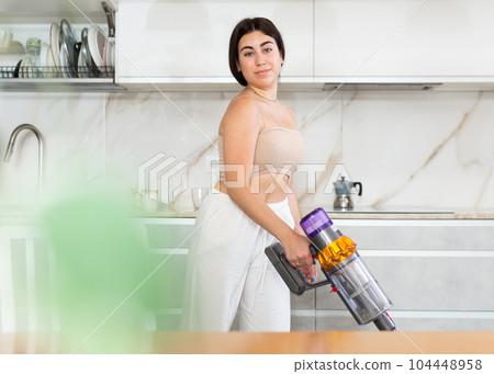 Positive young woman vacuum-cleaning the floor in the kitchen 104448958