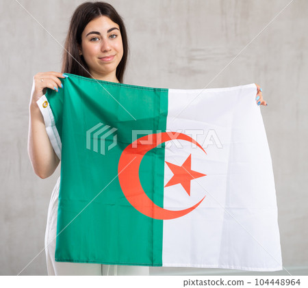 Happy young woman with flag of Algeria against unicoloured background 104448964