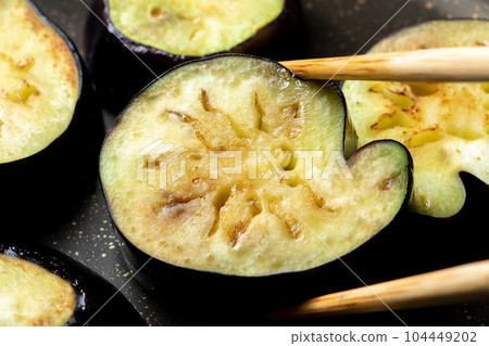 A cooking scene where eggplants are cut into round slices and baked in a frying pan. (Irregularly shaped eggplants harvested from a kitchen garden.) 104449202