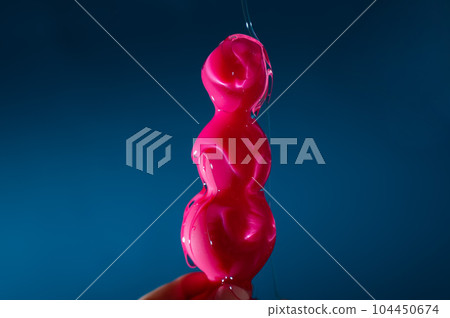 Woman pouring lubricant on pink anal beads on blue background.  104450674