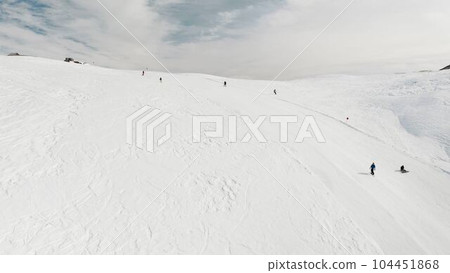 Livigno, Italy - February 21, 2022: People snowboarding skiing at ski resort. Skiers, snowboarders riding snowy mountain slope. Outdoor winter sport, scineric panoramic view. Aerial footage 4k 104451868