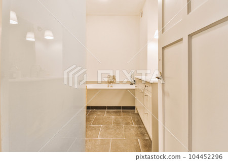 a bathroom with white walls and beige tile on the floor, there is an open door leading to another room 104452296